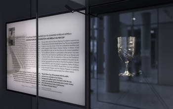 A glass case displaying the Spyros Louis Cup on the right and a plaque with information about the cup on the left.